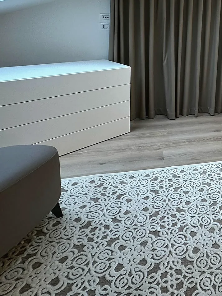 Damask-patterned rug on a pale floor, in front of a taupe wall-to-wall curtain