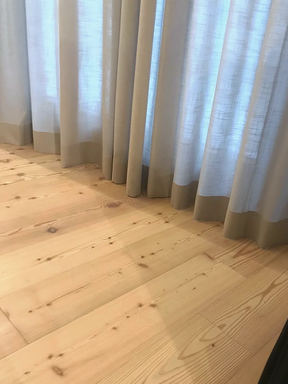 Pale curtains with a matching band at the hem, resting on a pine floor